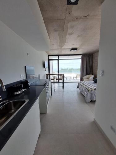 a kitchen with a sink and a room with a bed at Alquiler De Departamento Monoambiente Con Terraza, Frente Al Mar En La Costa Quequén, Con Pileta, Solarium y Sum Con Parrilla in Quequén