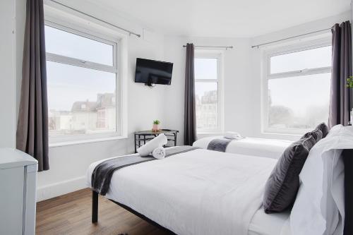 a white bedroom with two beds and two windows at Azure Beach Hotel in Bournemouth