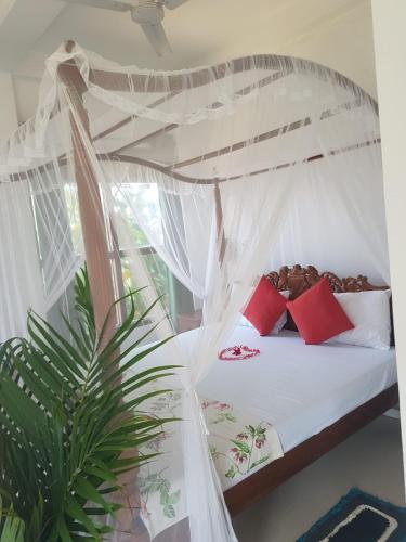 a bedroom with a white canopy bed with red pillows at Dreamvillage in Dodanduwa