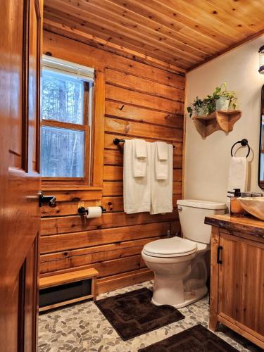 a wooden bathroom with a toilet and a window at Stylish Forest Lodge with Large Hot Tub, Firepit and Fireplace minutes to Gore Mountain in North Creek