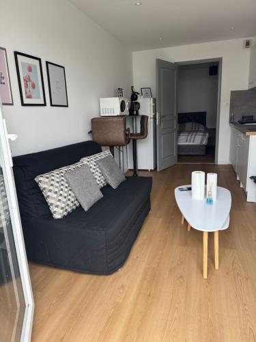 Una sala de estar con un sofá negro y una mesa. en Appartement 1 chambre vu sur jardin, en La Roche-sur-Yon