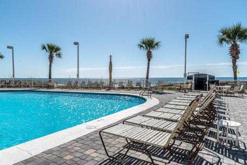 a pool with chairs and palm trees and the ocean at Tradewinds 908 in Orange Beach