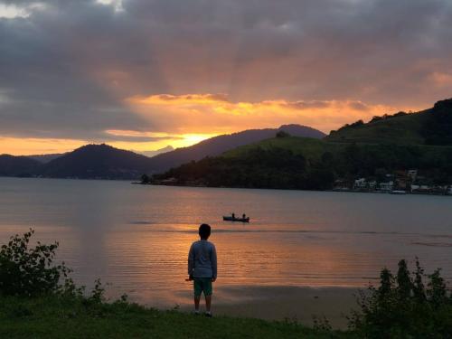 安格拉杜斯雷斯Casa de praia no paraíso de Angra!的日落时站在湖岸边的人