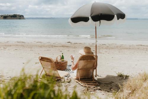 a person sitting in a chair under an umbrella on the beach at The Boatshed Big Manly in Whangaparaoa