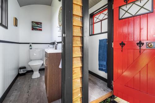 La salle de bains est pourvue d'une porte rouge et de toilettes. dans l'établissement Onaeros Cute Little Cottages - Taranaki Retreat, à Waitara