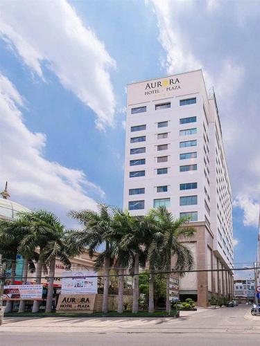 a tall white building with palm trees in front of it at AURORA Hotel Plaza in Bien Hoa