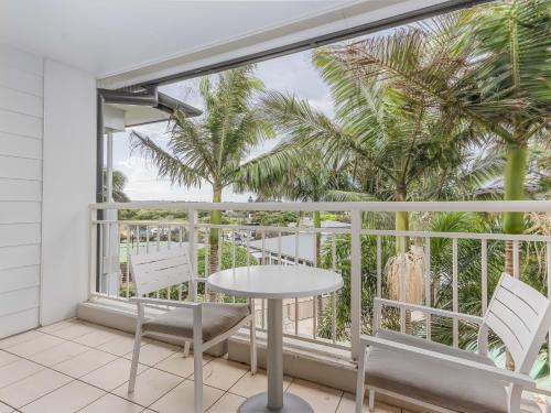 a balcony with a table and chairs and palm trees at The Pool Resort Kingscliff - Private Apartments by Holiday Management Company in Kingscliff
