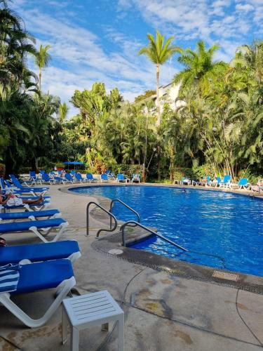 a resort swimming pool with blue lounge chairs and palm trees at 2 Bedroom Treetop Condo in Puerto Vallarta