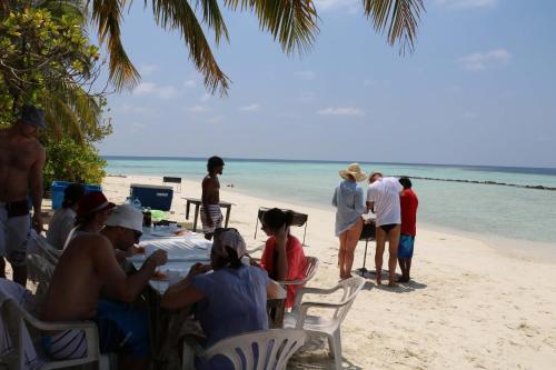 a group of people sitting at a table on the beach at Liberty Guesthouse Maldives in Mahibadhoo