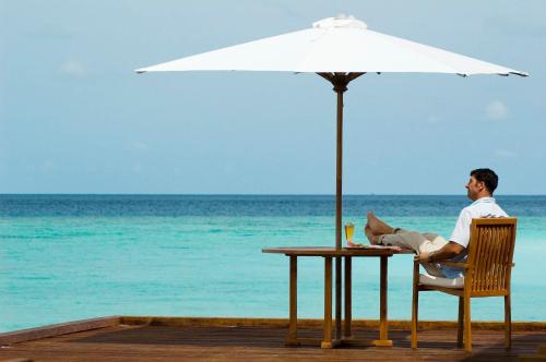 a man sitting at a table under an umbrella on the beach at Adaaran Prestige Water Villas - with Dine around Premium All inclusive - 24 hours in Raa Atoll