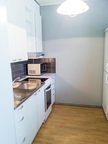 een kleine keuken met witte kasten en een wastafel bij Apartment Kukkarokivenkatu in Mänttä