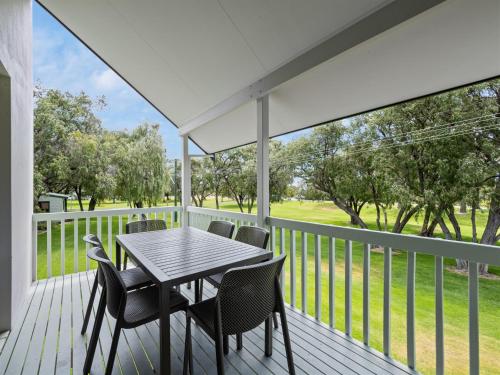 a table and chairs on a porch with a view of a golf course at Mandalay Holiday Resort and Tourist Park in Busselton