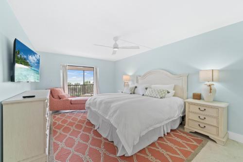 a white bedroom with a bed and a chair at Sanddollar #A202 in Ybel