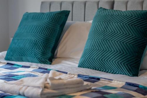 a bed with two green pillows and a blanket at Kerr Apartment-Spacious 4-Bed Flat in Hamilton, Close to Glasgow in Cadzow