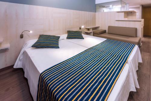 a large white bed with blue and yellow striped pillows at GHT Sa Riera in Tossa de Mar