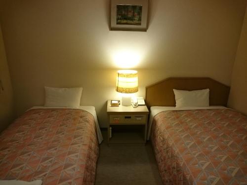 a hotel room with two beds and a night stand with a lamp at Hotel Lakeland Hikone in Hikone