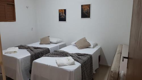 Zimmer mit 3 Betten mit weißen Tischen und Bildern an der Wand in der Unterkunft Casa de Praia Toca da Onça in São Miguel do Gostoso