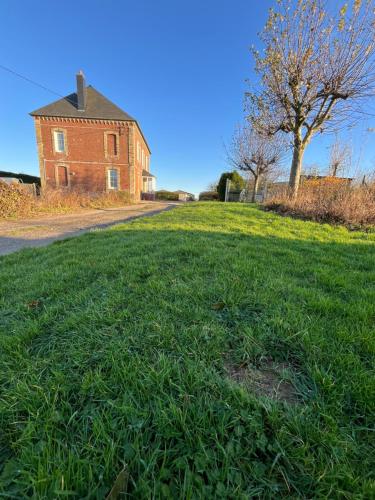 a large field of grass next to a brick building at Gîte familial à la ferme des Hellandes in Angerville-lʼOrcher