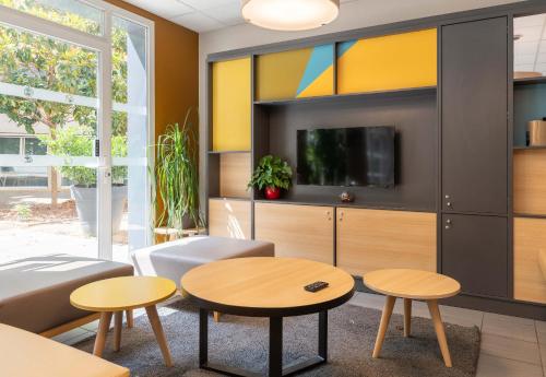 a living room with two tables and a tv at B&B HOTEL Lyon Caluire Cité Internationale in Caluire-et-Cuire