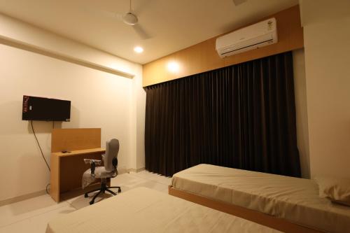 a bedroom with two beds and a desk and a window at Hotel Devbhoomi Prime in Khambhāliya