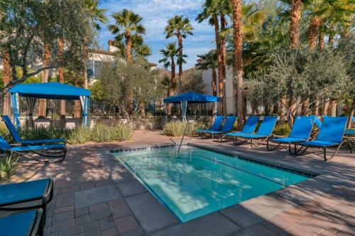 a swimming pool with blue chairs and trees at Modern LQ Getaway Steps to pool & spa #A in La Quinta