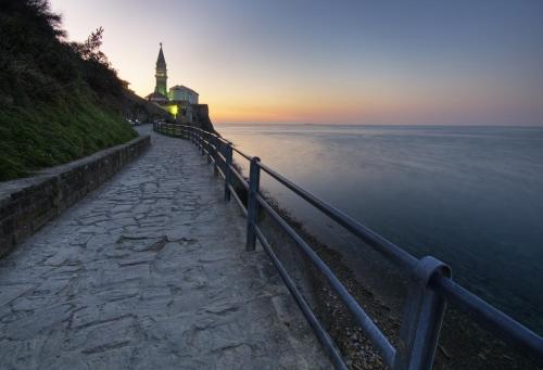 a path next to the water with a clock tower at Barbara Piran Beach Hotel in Piran