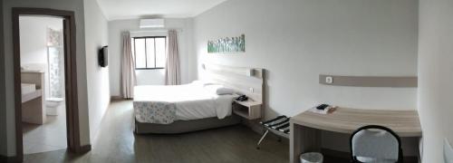 a white bedroom with a bed and a desk and a table at Hotel De Klomp in Carambeí