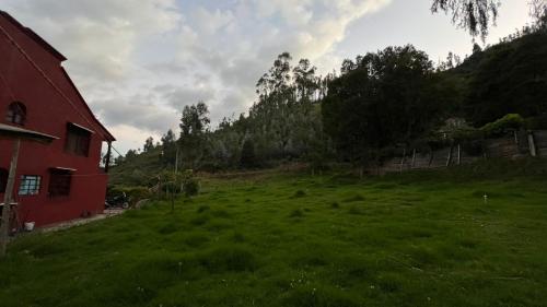 a large grassy field next to a red house at Cabaña San José in Tibasosa