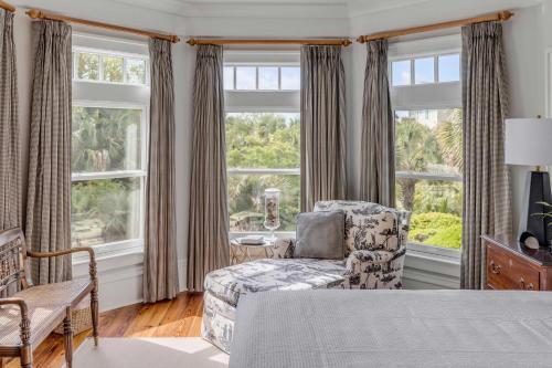 Un dormitorio con una cama y una silla y ventanas. en FW126: 126 Flyway Drive, en Kiawah Island
