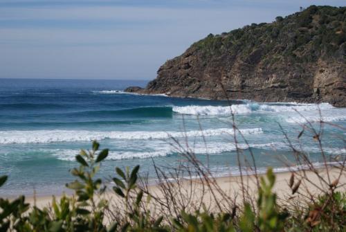 a beach with waves in the ocean next to a mountain at Beachside Haven Free Linen Wi-Fi Netflix air con in Boomerang Beach