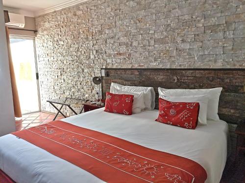 a bed with red pillows and a brick wall at Londiningi Guesthouse in Windhoek