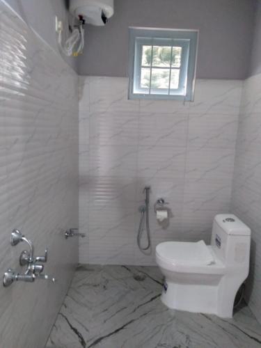 a white bathroom with a toilet and a window at Nidaya Sohra in Cherrapunji