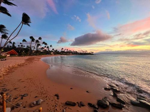 a beach with palm trees and the ocean at sunset at Kanai A Nalu 302 in Wailuku