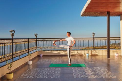 a man doing yoga on a green mat on a balcony at WelcomHeritage Natraj, Mcleod Ganj in McLeod Ganj