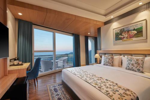 a bedroom with a bed and a desk and a large window at WelcomHeritage Natraj, Mcleod Ganj in McLeod Ganj