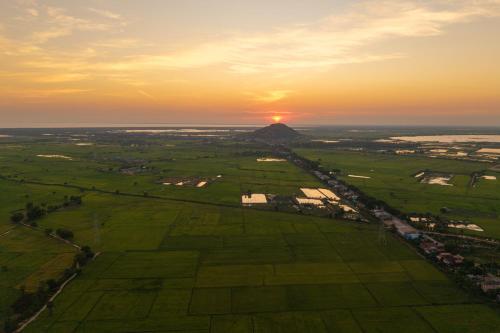 an aerial view of a field with the sunset in the background at Pomelo Outpost Cambodia ដំណាក់ភ្នំក្រោម in Phumĭ Rœssei Lŭk