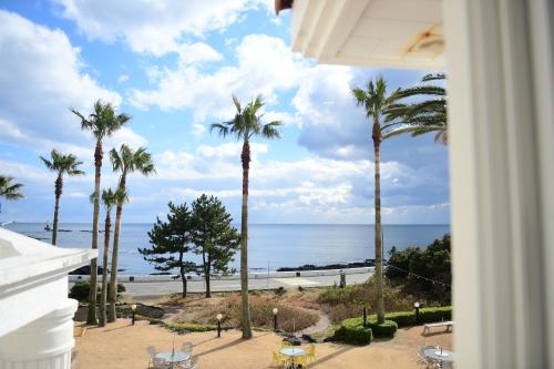 a view of the ocean from a building with palm trees at Jennyville Pension in Seogwipo