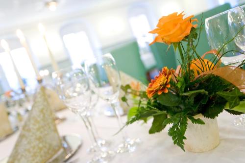 a vase with orange flowers on a table with glasses at Hotel Erbgericht in Bad Schandau