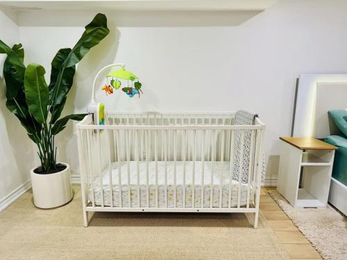 een witte wieg in een kamer met een plant bij 2 BR ground-level suite in a bungalow with full kitchen, parking, and 20 mins to Downtown in Toronto