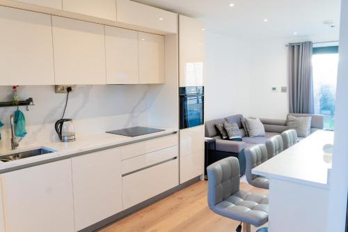 a kitchen and living room with white cabinets and a couch at Modern Entire Unit 3BR, 3BA, balcony, 86inch TV - 15mins to city in Romford
