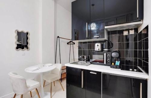 - une cuisine avec des appareils en noir et blanc, une table et des chaises dans l'établissement Charmant studio au cœur de paris, à Paris