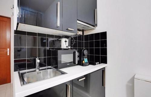 - une cuisine avec un évier et du carrelage noir sur le mur dans l'établissement Charmant studio au cœur de paris, à Paris