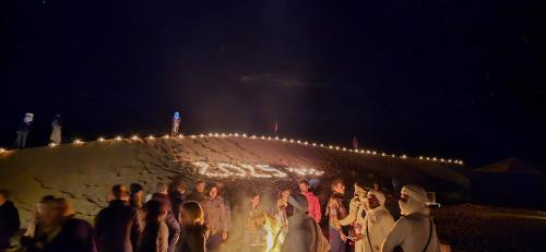 a group of people standing next to a wall with lights at Erg Chigaga Torza Luxury Camp - Desert Glamping in El Gouera