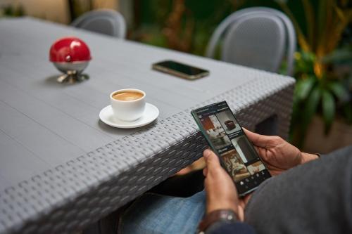 a person holding a cell phone and a cup of coffee at Le Jardin Privé in Alger