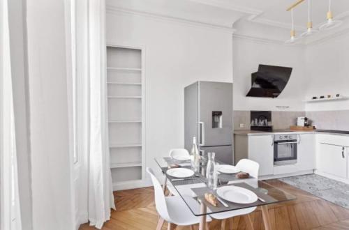 - une cuisine blanche avec une table en verre et des chaises blanches dans l'établissement Appartement Haussmannien Saint Michel Notre Dame, à Paris