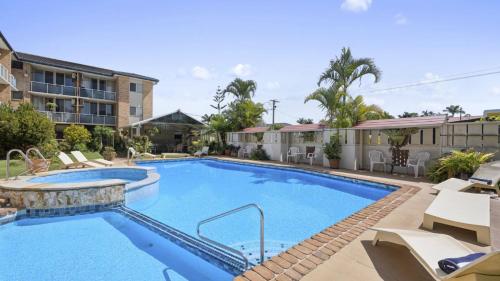 a large swimming pool with chairs and a building at Ocean Parade 4 - Affordable, Pool, Spa, Cafes, Sleeps 4 in Coffs Harbour