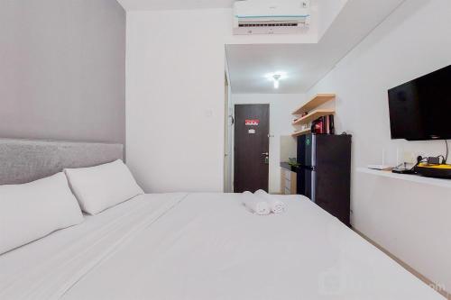 a bedroom with a white bed and a black refrigerator at Enjoy Living and Warm Studio at Serpong Garden Apartment By Travelio in Tangerang