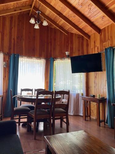 Un comedor con mesa y sillas y un televisor. en Cabaña en Coñaripe Sector Termas Geométricas "Entre Coigûes", en Coñaripe