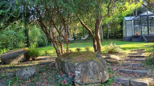 a garden with a rock and trees and a greenhouse at Camellia Grove Retreat in Mount Macedon