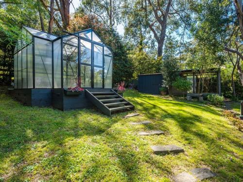 a greenhouse in the grass with a bench in a yard at Camellia Grove Retreat in Mount Macedon